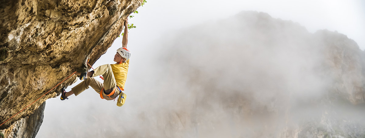 Escalador equipado con Petzl sobre roca, con montañas al fondo