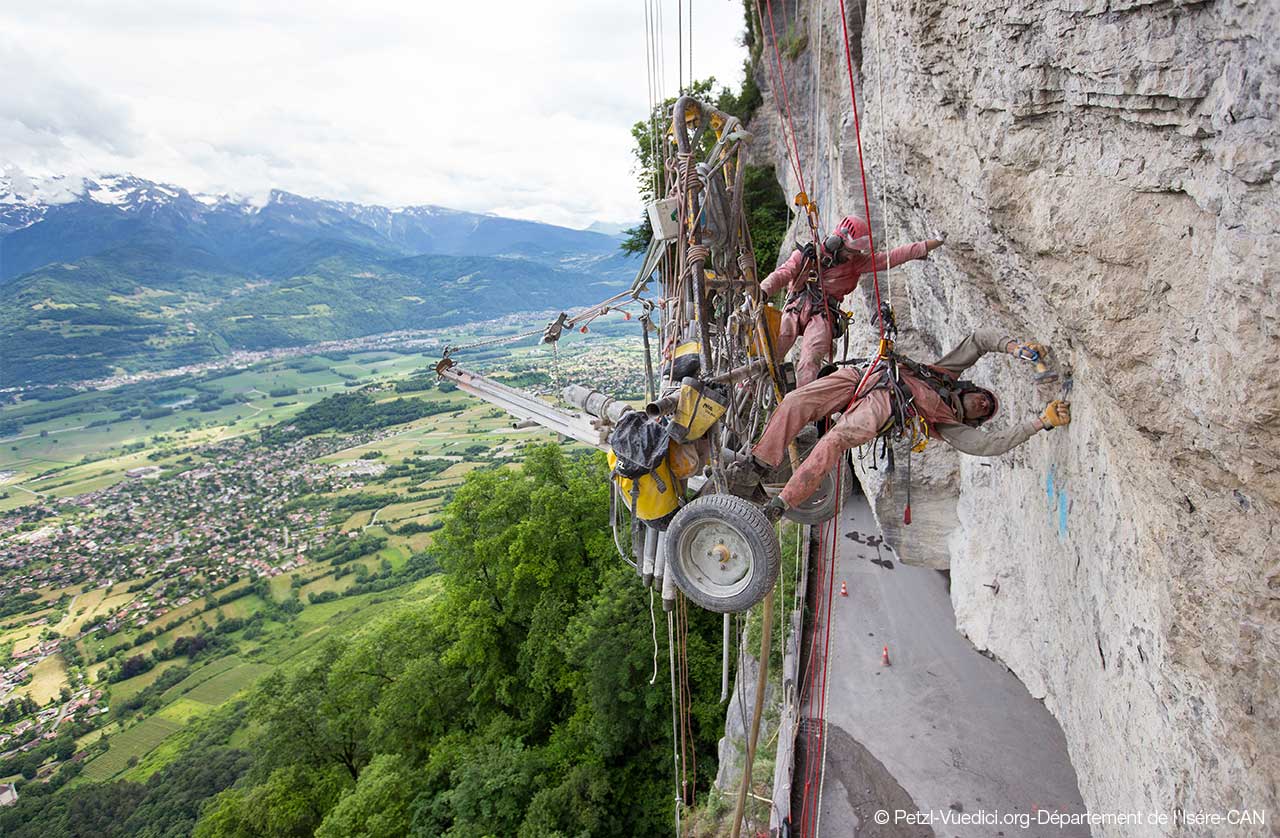 Operarios con equipos Petzl trabajando con una perforadora suspendida en un talud rocoso de Saint-Pancrasse, Francia